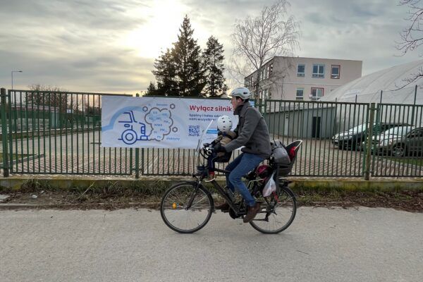 Father cycles with child in front of air pollution warning banner.