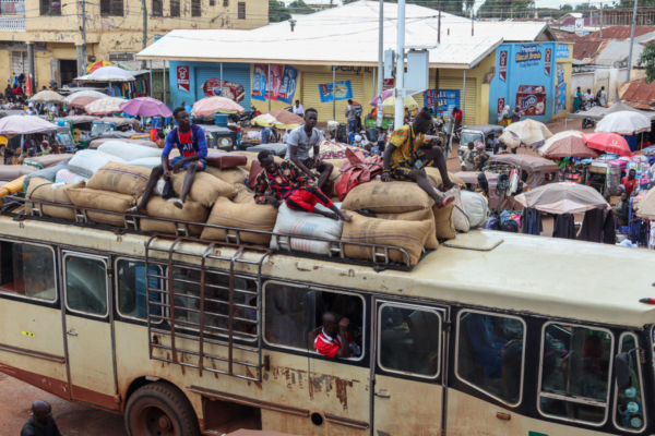 Men ride through an urban area in Ghana on top of a bus during a drought.