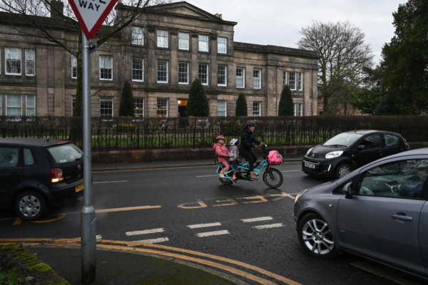 Woman cycles her children to school on a cargo bike, through busy traffic, in Didsbury, Manchester,