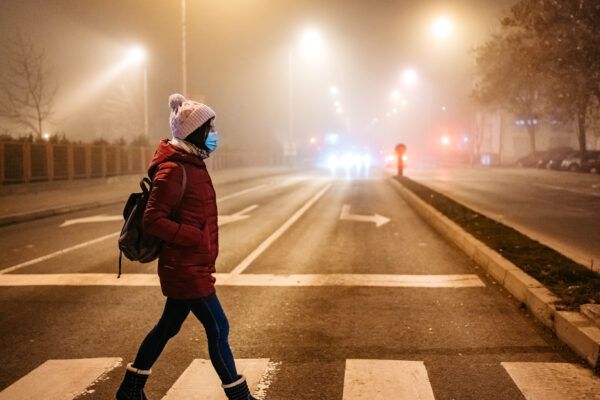 Young woman wearing face mask and crossing the street on pedestrian crossing in foggy night.
