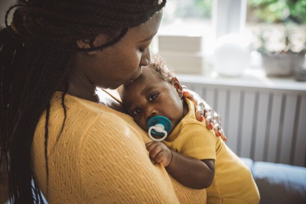 Smiling mom cuddle with small baby at home.